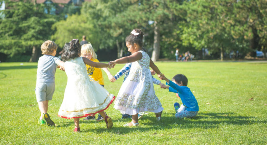 A group of children holding hands and swinging around in a circle in the grass