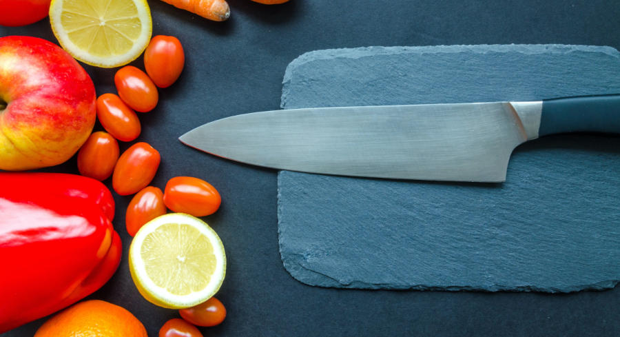 A knife and cutting board with vegetables on the side ready to be chopped and sliced