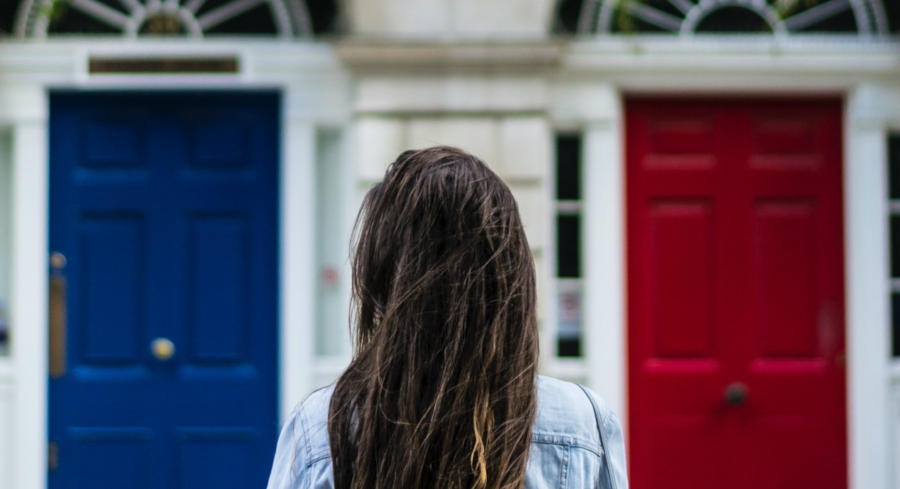 A woman stands before two doors and has to make a choice between one blue door and one red door