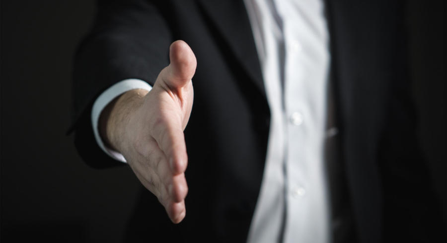 An image of a man offering his hand toward the screen for a handshake