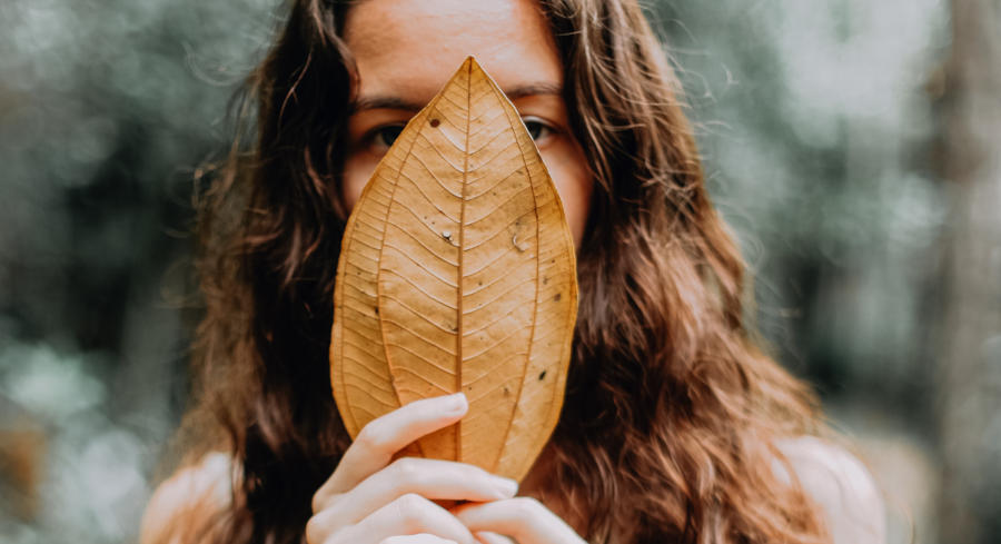 A woman holding a leaf in front of her mouth embarrassed.