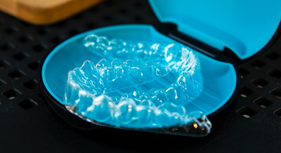 Two Invisalign clear aligner trays sitting inside of a blue aligner case
