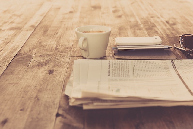 A cup of coffee, a newspaper, and a phone on top of a table