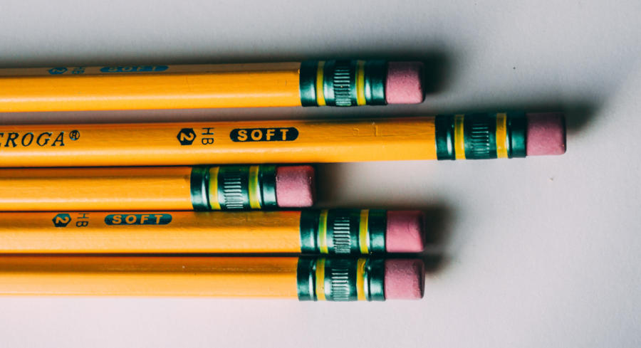 An assortment of yellow number 2 pencils with the camera focused on the pencil eraser