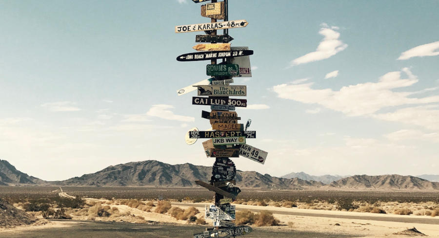 A massive roadsign post showing many different signs in the middle of the desert