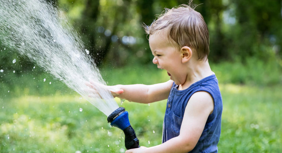 A child that is absolutely ecstatic to see water spraying up into the air from the hose spray