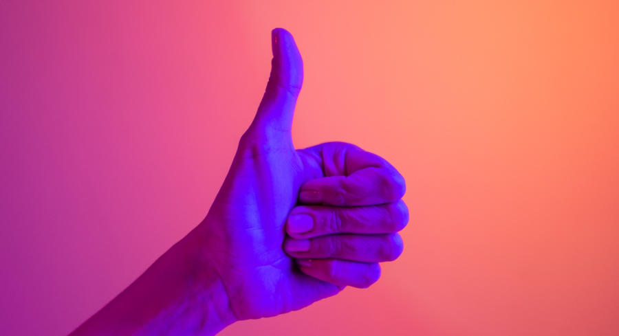 A hand in front of a screen giving a thumbs up sign