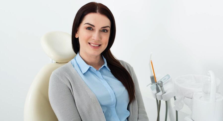 An attractive woman sits in a dental chair looking at the camera with a smile on her face