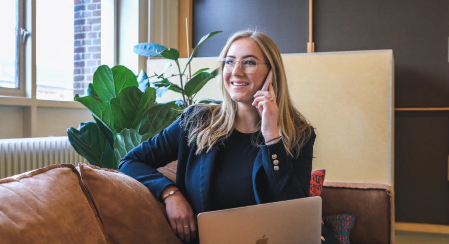 A woman holds her ear up to a phone as she sits in front of a computer