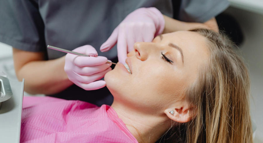 A woman lays back in a dental chair as an orthodontist checks her teeth